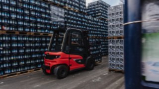 The Linde X30 electric forklift truck transports beverage crates through a narrow aisle in the outdoor storage area.