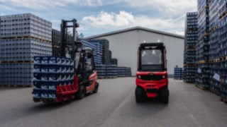 Two Linde electric forklift trucks are parked between stacks of crates in an outdoor premises.