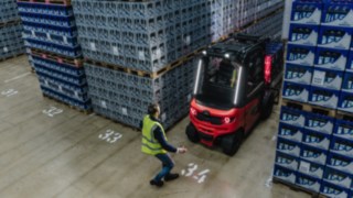 A Linde electric forklift truck reversed out of an aisle while a pedestrian is walking past.