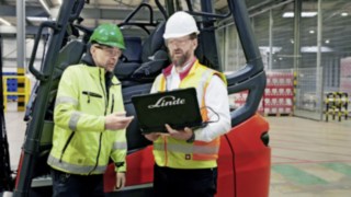 Two employees with a laptop standing in front of a Linde MH forklift truck