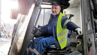 A forklift driver is sitting in a stationary Linde forklift truck and opening the door