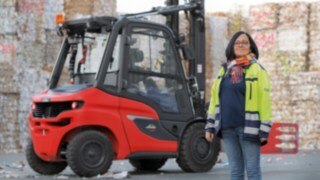 A woman is standing in front of a forklift truck in a plant