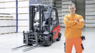A man with crossed arms is standing in a warehouse. There is a Linde forklift truck in the background. 
