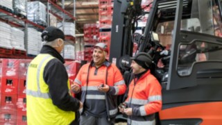 Three people talking in front of a forklift truck.