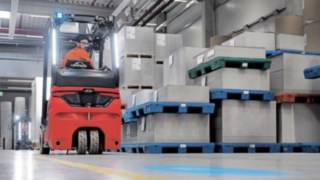 A forklift driver drives the Linde electric forklift backwards through a warehouse.